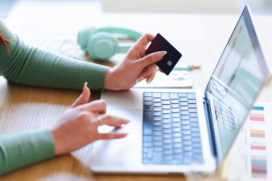 An Arab woman is shopping online using a credit card. She is using a laptop to make a purchase.