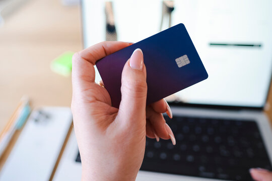 An Arab woman holds a Revolut Visa card. She is shopping online using her laptop.