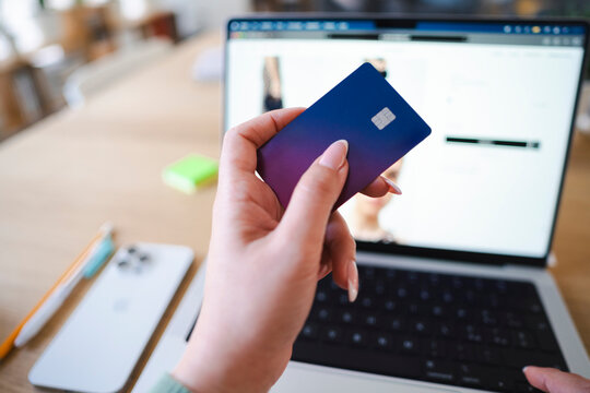 An Arab woman holds a Revolut Visa card while shopping online with a laptop. She is making a purchase on a website.