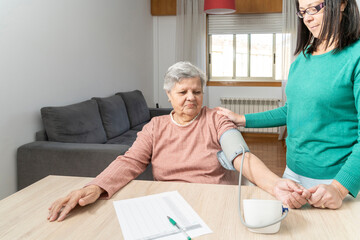 Obraz premium Daughter measuring her mother's blood pressure with a digital tensiometer at home