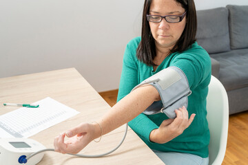 Woman adjusting blood pressure cuff on her arm, preparing to take a measurement with a digital tensiometer at home