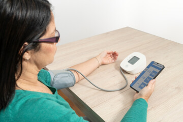 Woman using a wireless tensiometer to measure her blood pressure and checking the results on a smartphone app