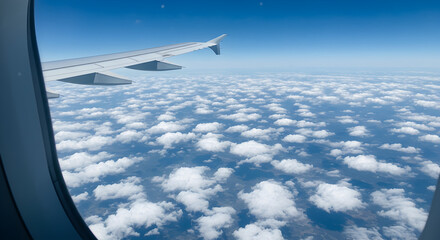 Fototapeta premium Aerial View From Airplane Window Reveals Clouds and Blue Sky with Plane Wing on the Left Side on Daylight