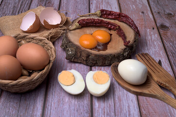 Rustic food composition with fresh eggs, egg yolks, boiled eggs, and dried red chilies on a wooden surface. Natural lighting and earthy tones create a warm, traditional kitchen atmosphere