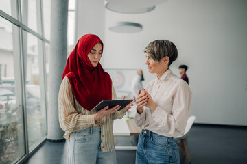 Two businesswomen discussing using digital tablet in modern office