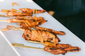 Grilled chicken skewers topped with sauce served on a platter at an outdoor event in sunny weather