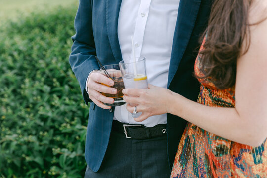 Couple holding drinks while enjoying a sunny outdoor gathering in a lush garden setting
