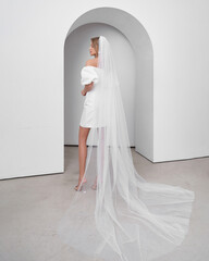 Blonde woman in wedding dress poses gracefully in bright interior with arch