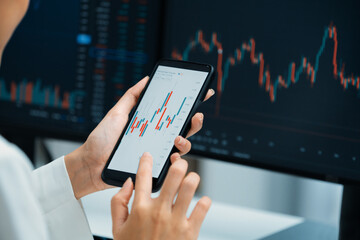 Cropped image in businesswoman using smartphone in profitable of exchange stock market graph comparing with pc screens at modern office. Concept of investing high profit in wealth security. Stratagem.