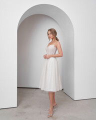 Blonde woman in wedding dress poses in bright interior with elegant archway