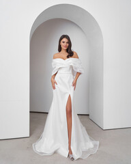 Brunette woman posing in a wedding dress in bright interior with an elegant arch