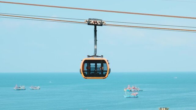 Modern cable car gondola ride over tropical seaside with fishing boats and turquoise sea on Phu Quoc island, Vietnam at Sunset town. Hon Thom cable car cabin. Tourism technology and infrastructure
