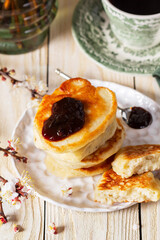 Lenten yeast pancakes with plum jam and tea, and a bouquet of flowering apricot branches on a light wooden table.