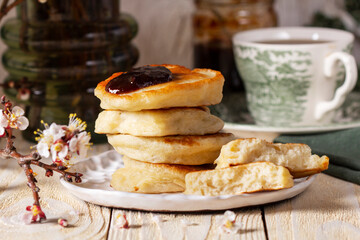 Lenten yeast pancakes with plum jam and tea, and a bouquet of flowering apricot branches on a light wooden table.