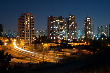 Cityscape at night with illuminated buildings and light trails from vehicles on the road below