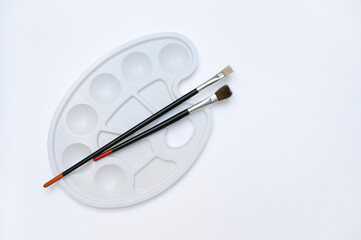 Isolated top view of paintbrushes and white plastic palette on a clean background. Perfect for art supply catalogs, school designs, creative tutorials and visual templates.