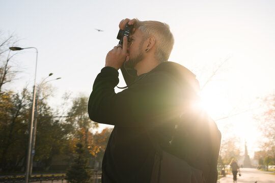 Backlit outdoor photo of a person using a camera in warm sunlight.
