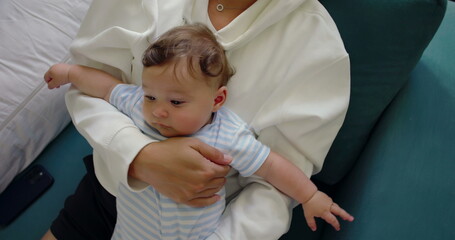 Close-up of baby lying comfortably on mother's lap, being held with care and affection in a warm...