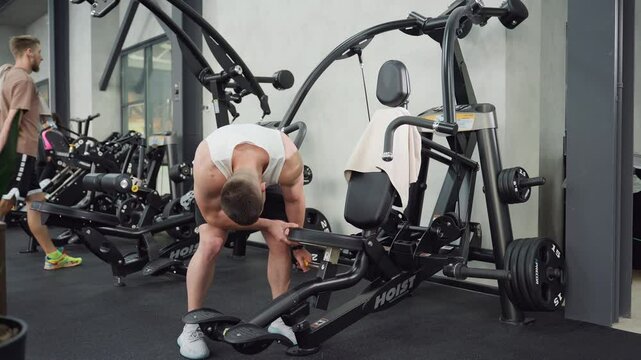 Weight lifter adjusts machine seat then sits gripping handle firmly, body engaging muscles under gym lighting as he positions for intense chest press workout on sleek equipment with dynamic motion