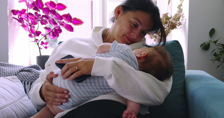 Mother smiling warmly at her baby while holding them in her arms, creating a tender and nurturing...