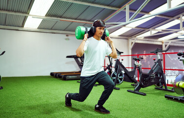 Young athlete doing lunges with power bag in modern gym