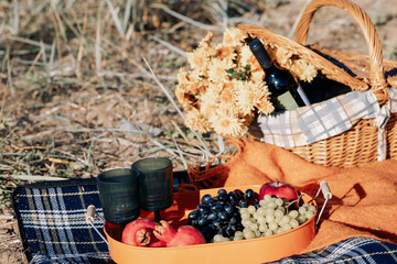 Autumn picnic on beach by sea. Fresh fruits, wine glasses, bottle, grapes, pomegranate near picnic basket on orange blanket. High quality photo