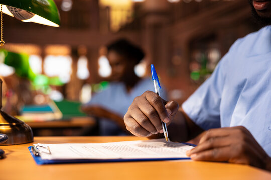 African american medical scholar creates a summary of class notes to learn easily for an exam, collecting information from the library to complete his knowledge. Future medic at desk. Close up.
