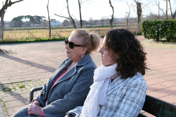 Woman and elderly mother sitting on a park bench enjoying the winter sun