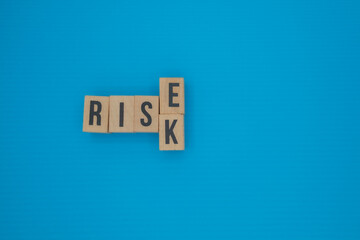 Wooden blocks with the words RISE and RISK on blue background, contrast between growth and...