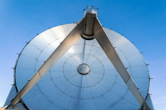 The shiny metallic surface of a radio telescope dish set against a clear blue sky