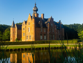 Obraz premium View of historical building of medieval castle in Flemish town of Rumbeke reflecting in water of pond on sunny summer day, Belgium..