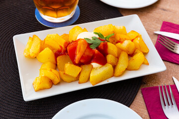 Prepared patatas bravas with sauce served on plate on wooden table