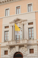 Vatican City flag waving on balcony of official building with neoclassical architecture in Rome Italy symbolizing Catholic Church and Holy See presence. High quality photo