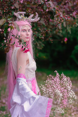 Deer dryad girl against the background of a blooming pink apple tree