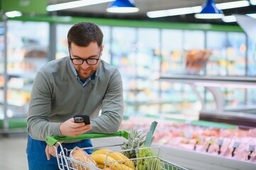 Happy man using mobile phone app while buying groceries in supermarket © Serhii