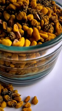 Golden yellow fenugreek seeds and other spices piled high in a clear bowl and scattered on a white surface, top-down view