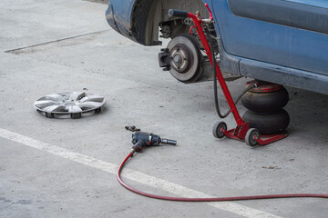 Close-up of seasonal tire change in progress: blue car on air jack, wheel removed, brake disc...