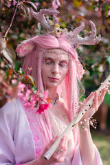Deer dryad girl against the background of a blooming pink apple tree