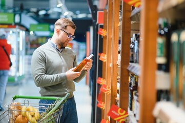 A man takes alcoholic drinks from the supermarket shelf. Shopping for alcohol in the store