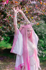 Deer dryad girl against the background of a blooming pink apple tree
