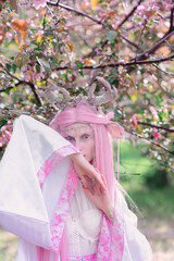 Deer dryad girl against the background of a blooming pink apple tree