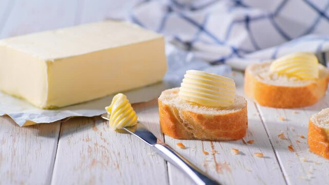Cut slice baguettes with curls butter on a light kitchen table. Sliced baguette with curls butter on a white kitchen table.