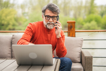 senior man sit on the terrace work on laptop and talk on mobile phone