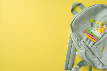 Green backpack with school stationery including scissors and pens on a bright yellow background