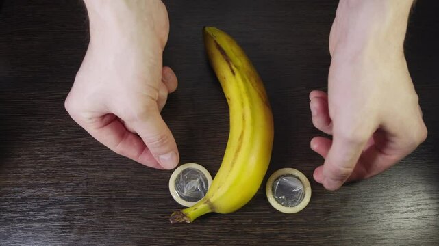 On the table is a banana in the shape of a phallic symbol, and on both sides of it are round condoms without packaging