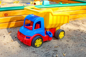 Bright red and yellow toy dump truck parked on sandy ground in outdoor children's playground area