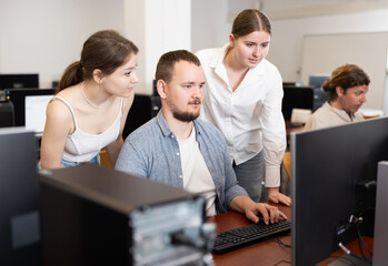 Young man and two young women colleagues discussing work at computer in office