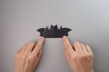 Scalloped bat wings folded by hands during Halloween craft process, hands-on step in DIY bat...