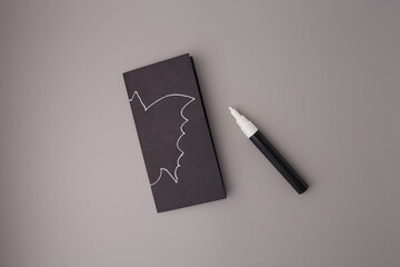Bat shape sketched on black rectangle with white marker, preparation stage of Halloween paper craft for kids, great for DIY blogs, creative kits, teaching tools, hobby brands, party assets,