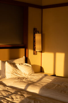 Golden morning light and shadows on the wall of a luxury hotel with unmade bed in southeast Asia. 
